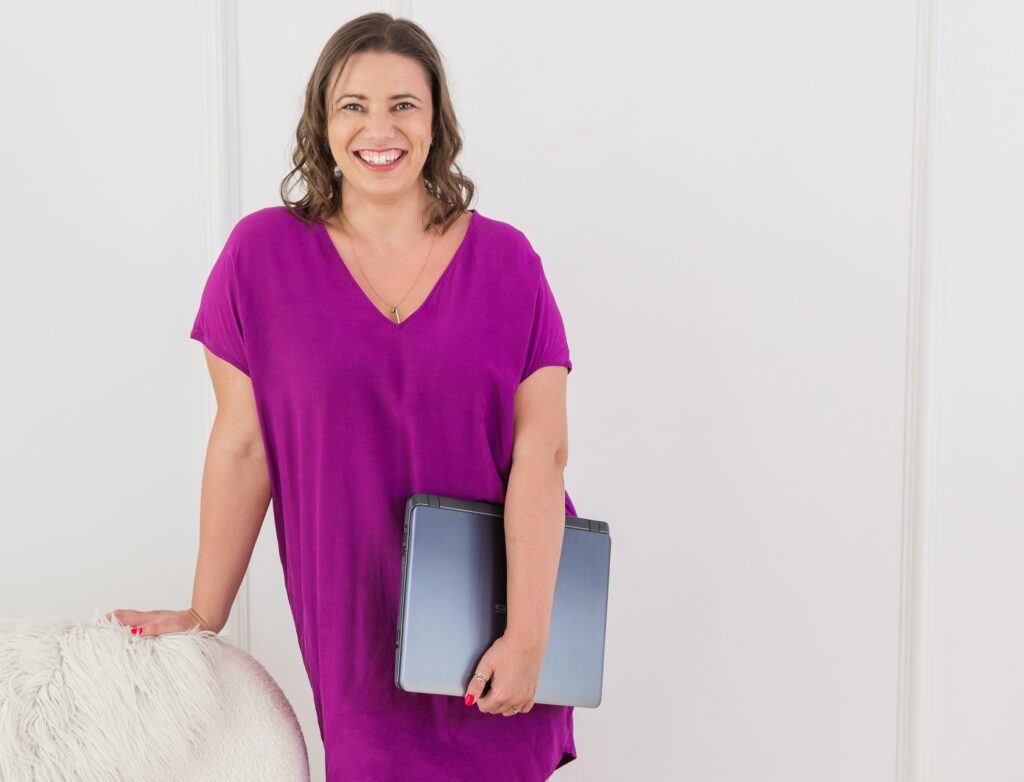 The author in a purple dress, holding a laptop casually in one hand, representing writing your own way and not having to have a daily writing habit